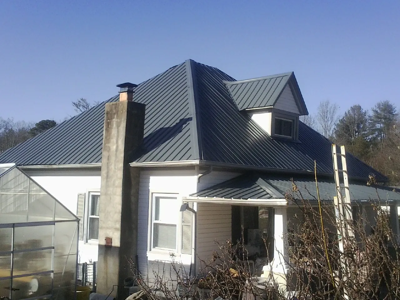 Dark blue standing seam metal roof on a white farmhouse with dormer — Slate & Tile Roof Repair by Roofing Brothers in Southgate