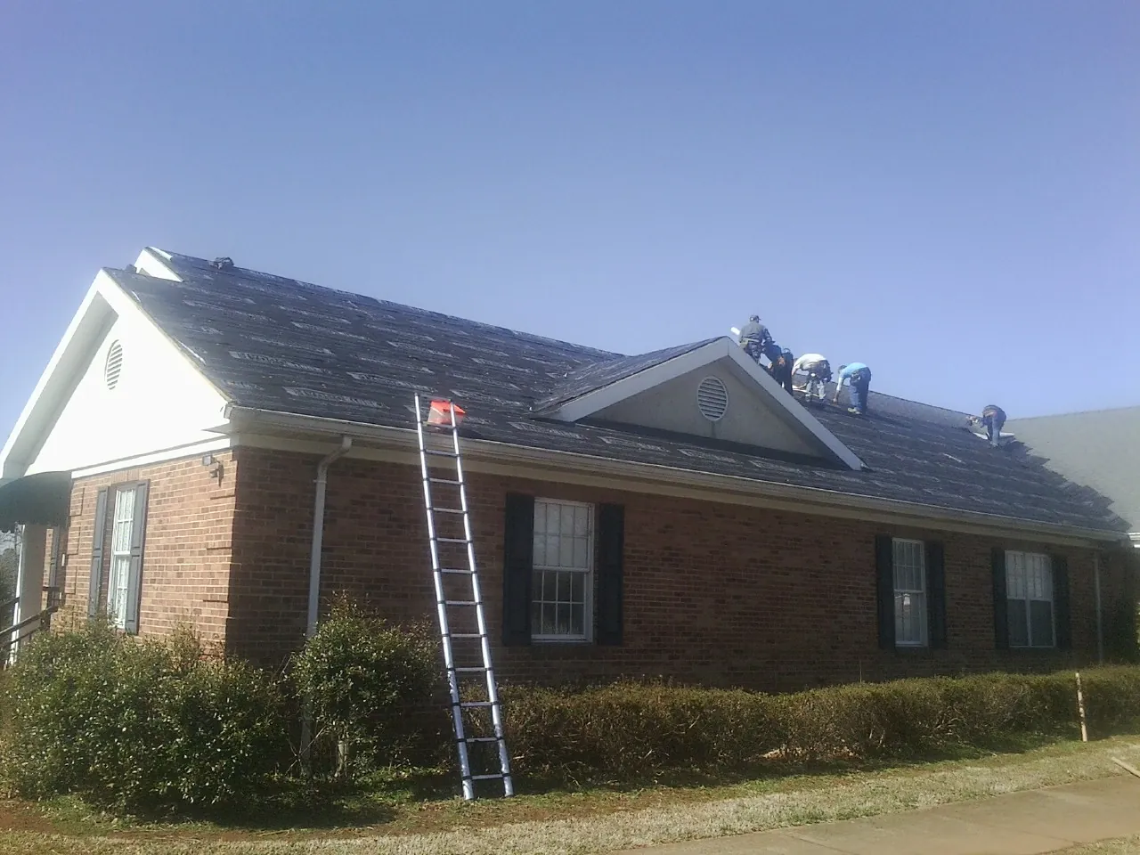 Crew tearing shingles off a brick ranch roof with a ladder set — Metal Roof Repair work by our crew in Southgate