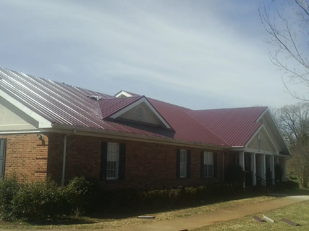 Red metal roof with gabled entries on a long brick building, from a Hail Damage Roof Repair job in Southgate