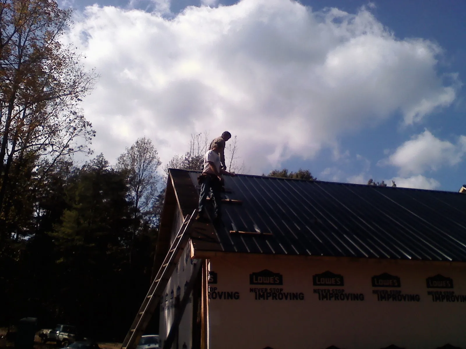 Roofer fastening dark metal panels high against a cloudy sky, from a Roof Inspection job in Southgate